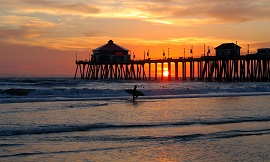 Surfer Silhouette In Foreground of Pier At Sunset
