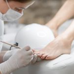 Professional in beauty salon cleaning nails on feet.