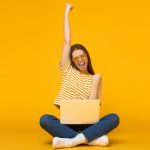 She is a winner! Excited young female with laptop isolated on yellow background