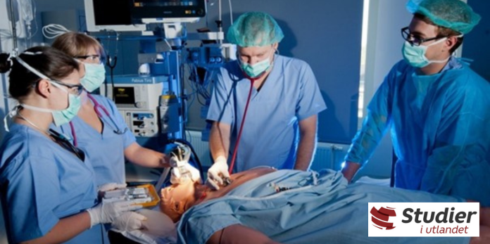 Bilde av fire medisinstudenter ved en sykehusseng. I sengen ligger en dukke, som de undersøker. Foto